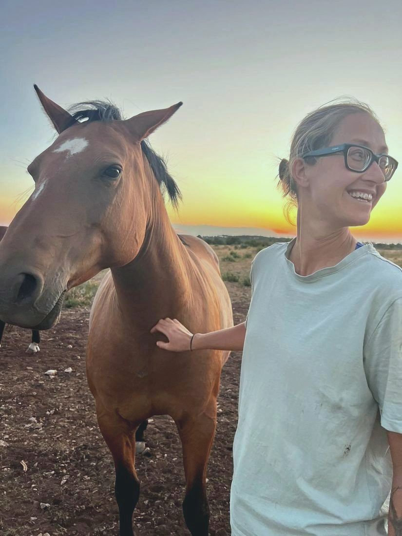 A woman smiling beside a horse at sunset